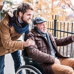 An elderly man in a wheelchair with his son acting as carer