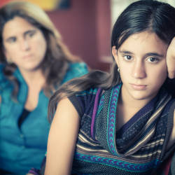 Overlooked by a worried Mother, a disinhibited child looks towards the camera, illustrating that disinhibition can be a subtle symptom of brain injury