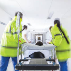 Medics rush a patient in a hospital bed to an operating room illustrating the NHS Costs Recovery Scheme