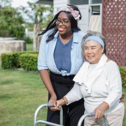 A carer guides an elderly lady with a walking frame illustrating our article on how much care is too much?