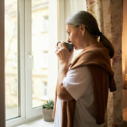 A lady looks out of the window whilst sipping a cup containing a hot drink illustrating the potential for missed diagnosis with a secondary brain injury