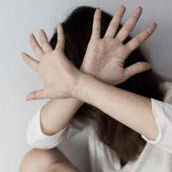 A lady shields her face, as if from a violent assault, illustrating our article on compensation for injuries sustained in violent assaults